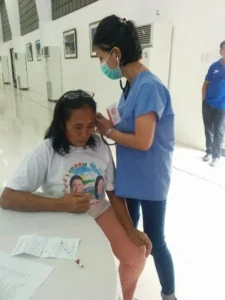 Healthcare worker wearing a mask assisting a seated woman in a clinic hallway